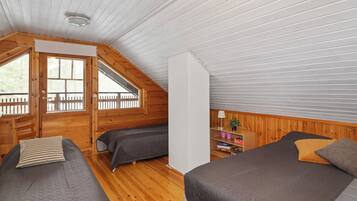 Une cabine avec deux lits, un plafond en bois et une fenêtre donnant sur une terrasse en bois.