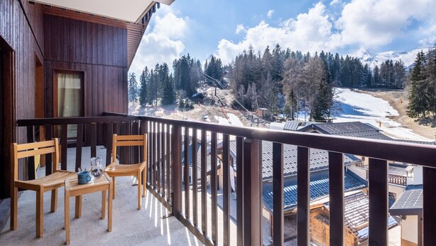 A balcony with wooden chairs and a table, overlooking a snowy landscape with trees and buildings. - Studio 4 ppl near the ski runs, ski lifts at 50m (Doucy)