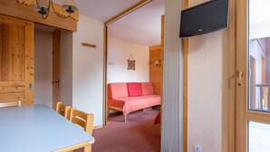 A room with a wooden table and chairs, a bed with a pink bedspread, a TV mounted on the wall, and a window. - Studio 4 ppl near the ski runs, ski lifts at 50m (Doucy)