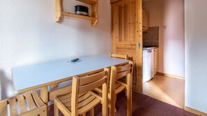 A wooden dining table with chairs, a small shelf with a pot, and a kitchen area with wooden cabinets and a stove. - Studio 4 ppl near the ski runs, ski lifts at 50m (Doucy)