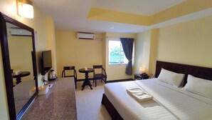 Ein Hotelzimmer mit Bett, Schreibtisch, Stuhl, kleinem Tisch, Spiegel, Klimaanlage und einem Fenster mit Vorhängen.