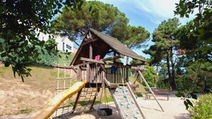 A playground with a slide, climbing wall, and a wooden playhouse.