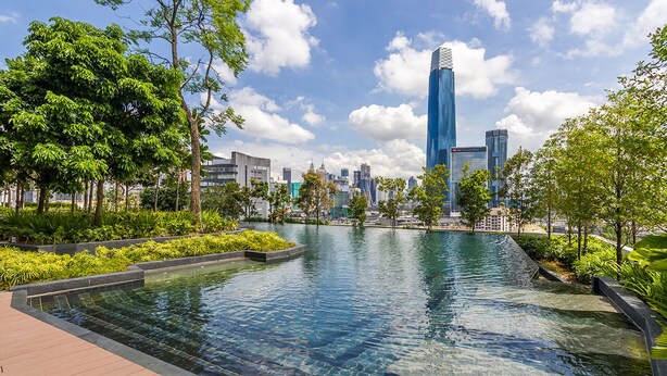 A swimming pool with a wooden deck, surrounded by greenery and modern buildings in the background. - Continew Residensi by Airhost  (Kuala Lumpur)