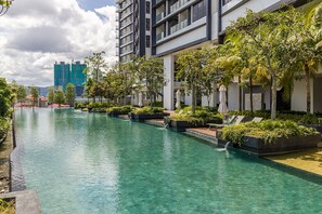 Un hôtel moderne doté d’une piscine, entouré de verdure et avec un immeuble de grande hauteur en arrière-plan.