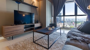 A modern living room with a flat-screen TV, wooden furniture, a coffee table, and a large window offering a city view. - Continew Residensi by Airhost  (Kuala Lumpur)