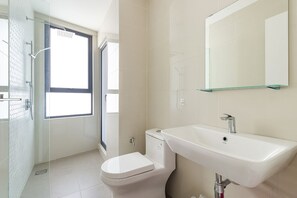 Une salle de bain moderne avec une douche à parois de verre, des toilettes blanches et un grand lavabo surmonté d’un miroir.