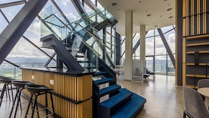 A modern interior with a glass staircase, wooden accents, and a view of the city. - Continew Residensi by Airhost  (Kuala Lumpur)