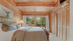 A wooden cabin bedroom with a bed, a nightstand, a lamp, and a window with a view of trees. - Private Hot Tub _ Pet Friendly _ 2 Living Rooms + Kitchen & Kitchenette (Vail)