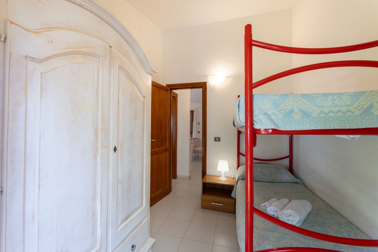 Une chambre avec un lit superposé, une armoire en bois et une petite table de chevet avec une lampe.