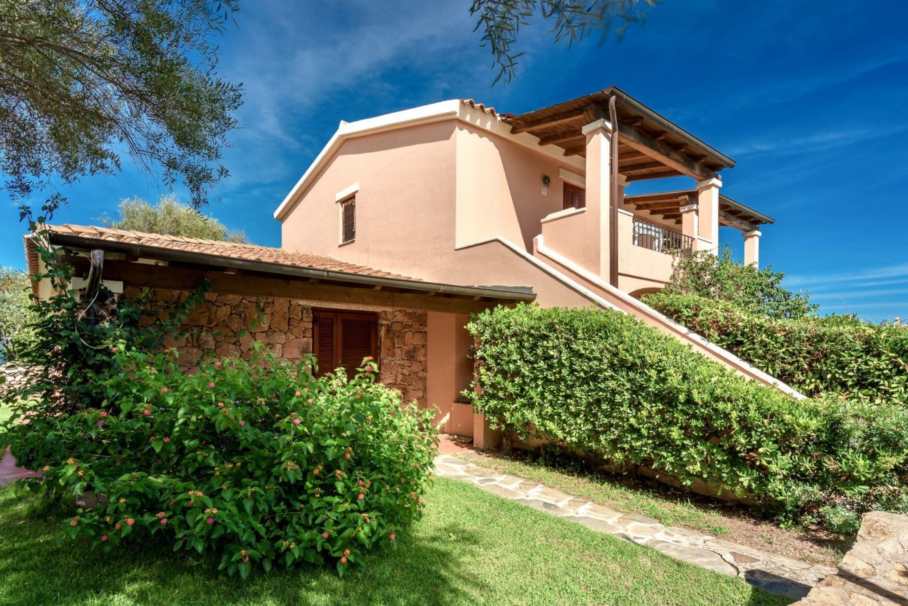 A two-story house with a stone facade, a wooden balcony, and a stone pathway leading to the entrance.
