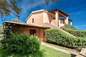 A two-story house with a stone facade, a wooden balcony, and a stone pathway leading to the entrance.