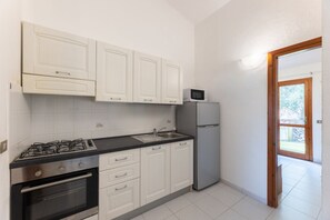 A kitchen with white cabinets, a gas stove, an oven, a sink, a microwave, and a refrigerator.