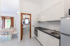 A modern kitchen with white cabinets, a black countertop, and stainless steel appliances. There is a dining area with a table and chairs.