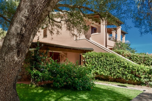 A two-story house with a stone facade, a balcony, and a well-maintained garden.