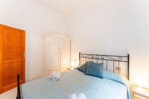 Et soveværelse med en seng, en træskab, et hvidt skab og et natbord med en lampe.