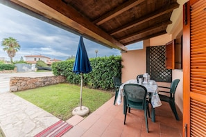 An outdoor patio with a table and chairs, a blue umbrella, and a stone wall.