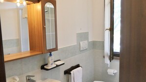 Een badkamer met een houten wastafelmeubel, een spiegel, een wastafel, een toilet en een raam met gordijnen.