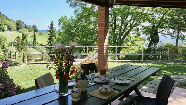 Een terras buiten met een eettafel, een bakstenen pilaar en uitzicht op een groen landschap.