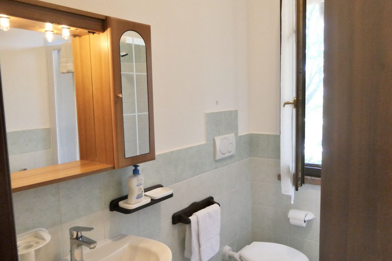 Een badkamer met een houten wastafelmeubel, een spiegel, een wastafel, een toilet en een raam met gordijnen.