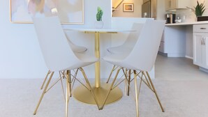 Un coin repas avec une table et des chaises blanches, un pied de table doré et un cactus en guise de centre de table.