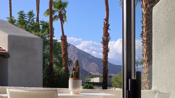 Un balcon avec deux chaises blanches, un cactus dans un pot et une vue sur la montagne.