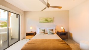 Une chambre d’hôtel moderne dotée d’un grand lit, d’un ventilateur de plafond, d’un balcon avec une porte vitrée et d’une vue sur l’extérieur.