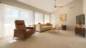 Un salon spacieux comprenant un fauteuil en cuir, un canapé, une table basse et un ventilateur de plafond.