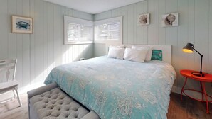 Un dormitorio con cama, una silla, un banco, un escritorio y una lámpara.