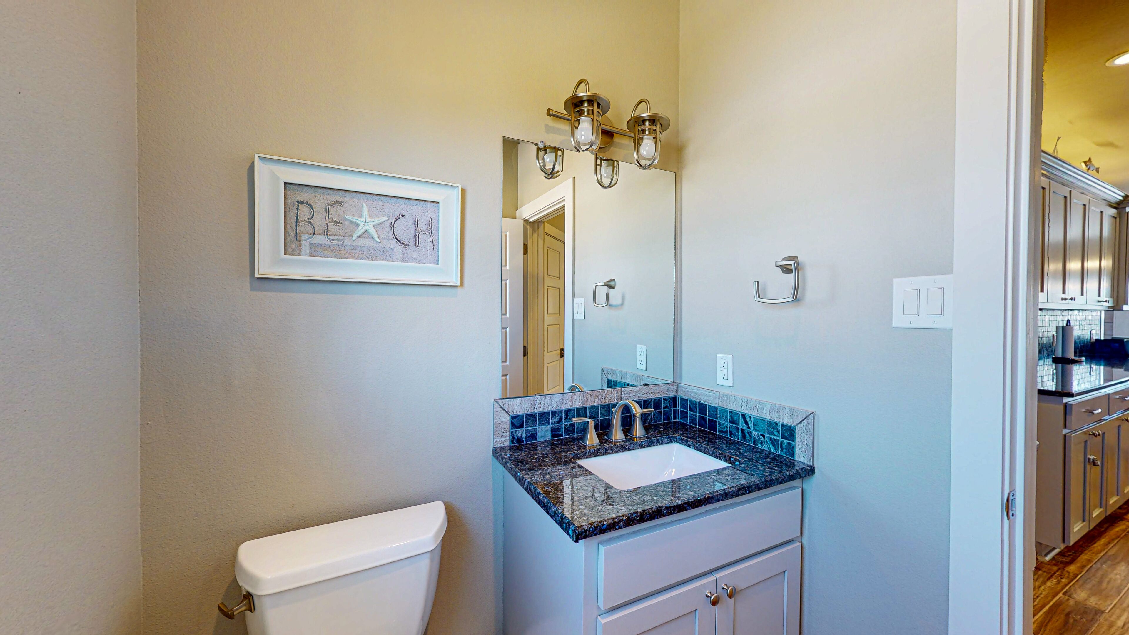 A bathroom with a white toilet, a sink with a blue and gray marble countertop, and a mirror above the sink.