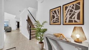 Stairs lead to an upper level, surrounded by abstract artworks and a minimalist reception area.