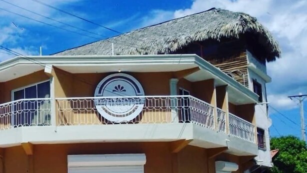 Um edifício de dois andares com telhado de palha, uma varanda com grades brancas e um logotipo circular na fachada.