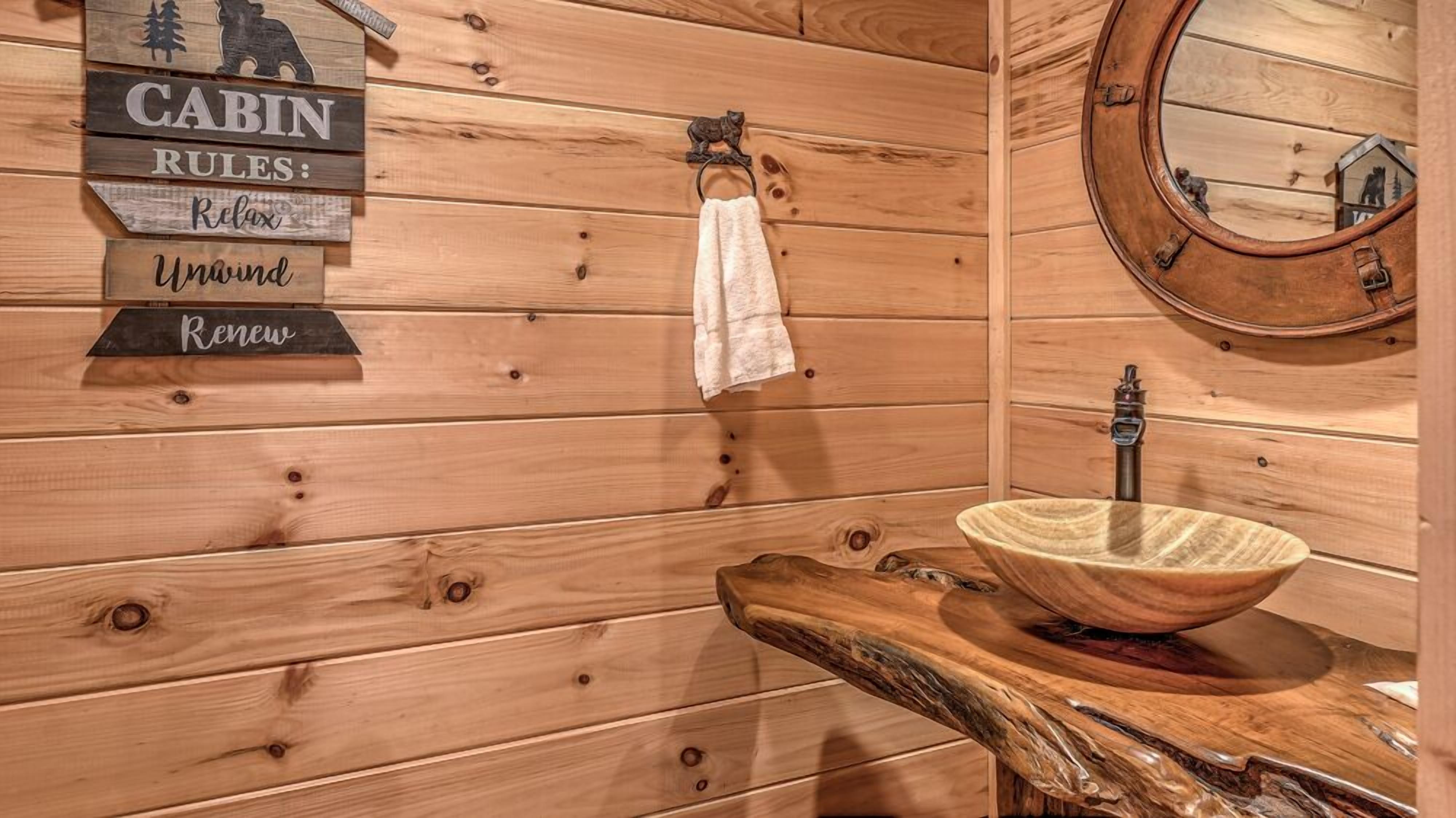 L’intérieur d’une cabine avec des murs en bois, un lavabo en bois avec un récipient, une serviette suspendue à un crochet et un panneau indiquant les règles de la cabine.