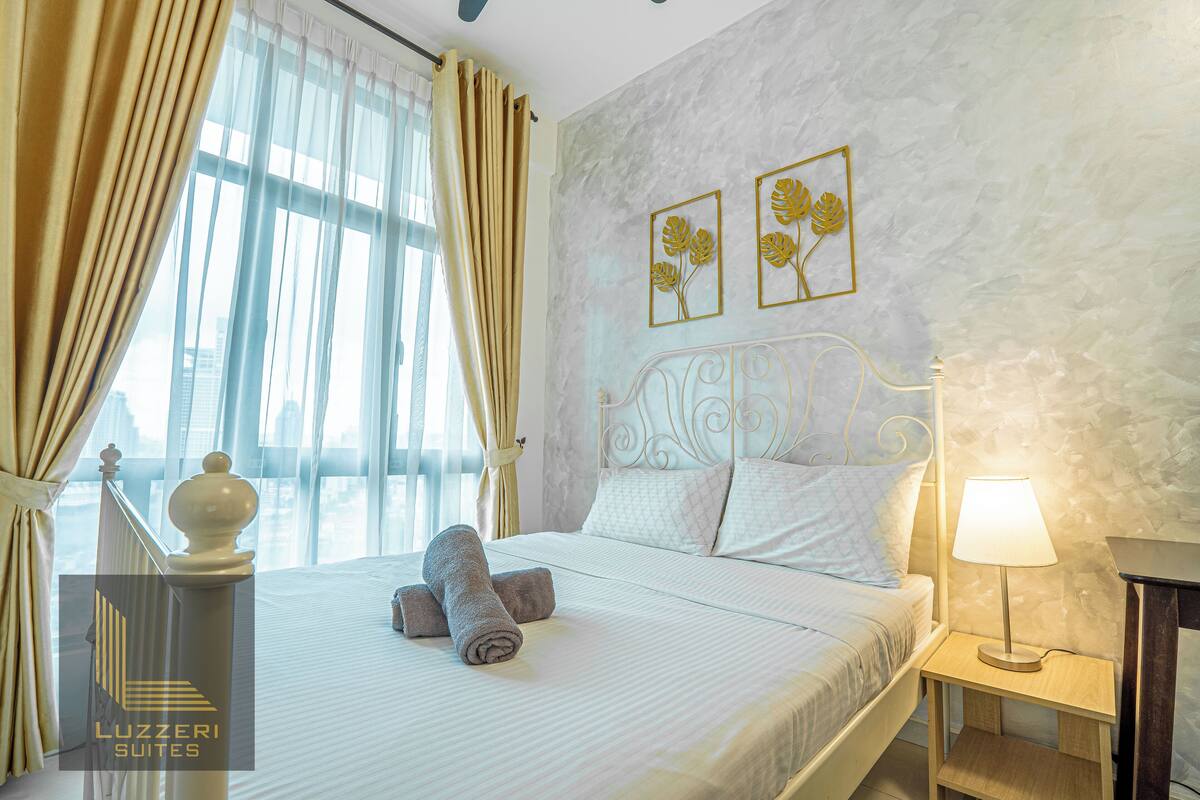 Une chambre d’hôtel avec un lit, des rideaux, une table de chevet avec une lampe et deux œuvres d’art accrochées au mur.