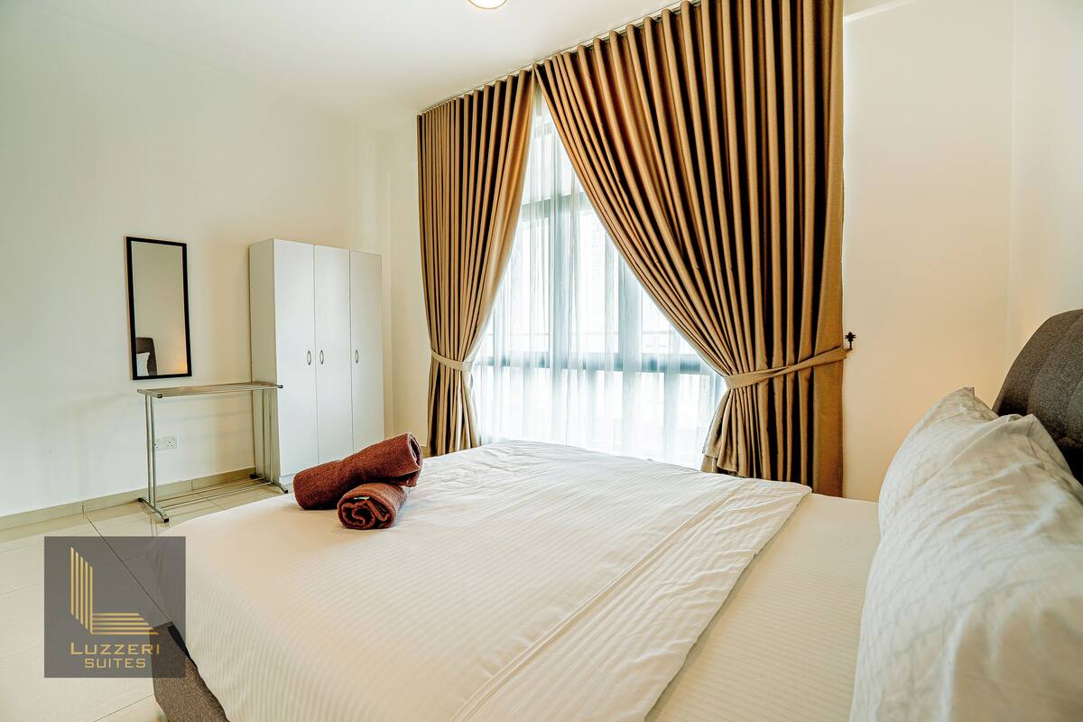 Une chambre d’hôtel avec un grand lit, une armoire, un miroir et une fenêtre avec des rideaux.