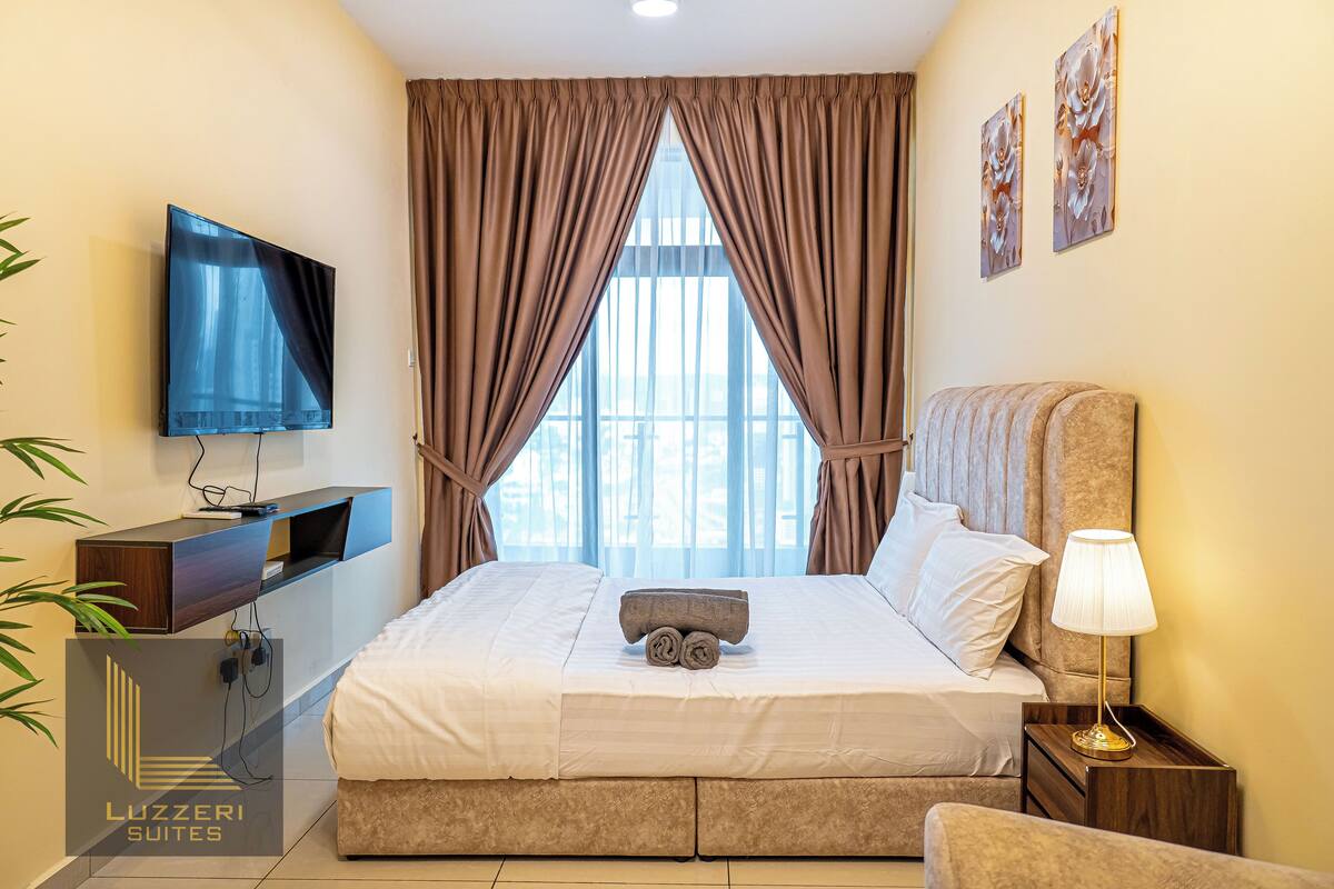 Une chambre d’hôtel avec un lit, une télévision, une table de chevet avec une lampe et une fenêtre avec des rideaux.