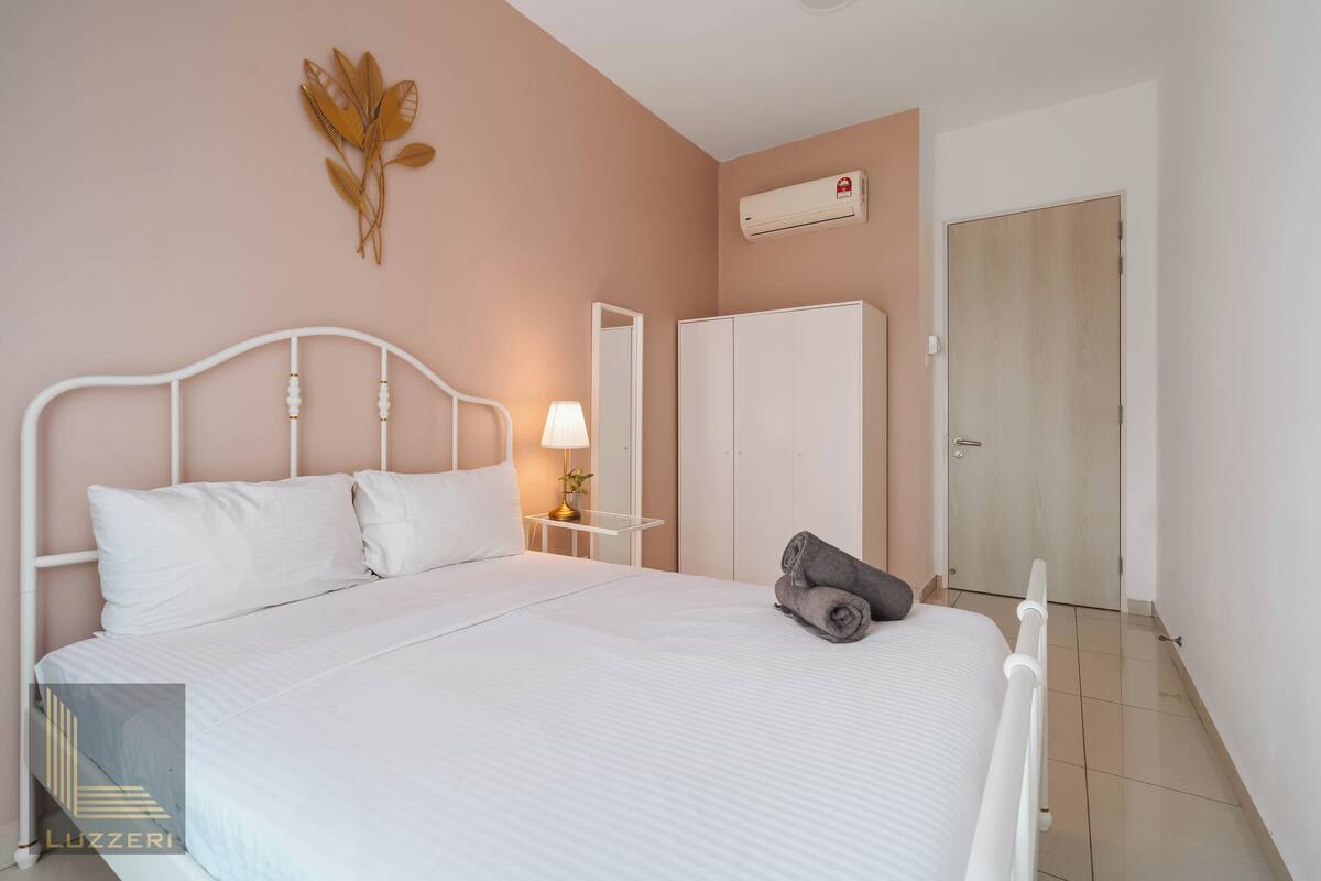 Un lit bien fait, avec une literie blanche, une lampe de chevet, une serviette enroulée, une armoire et un appareil de climatisation fixé au mur.