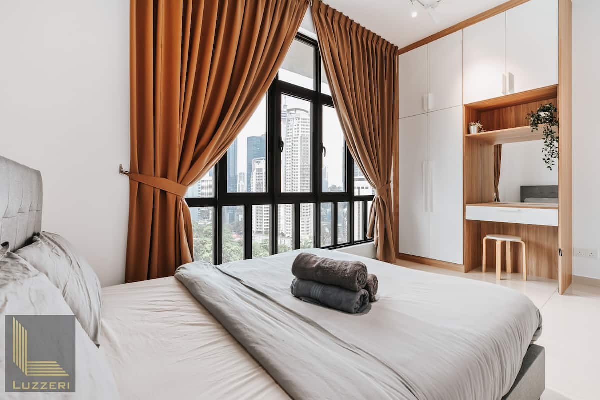 Une chambre moderne avec un grand lit, un bureau et une vue sur la ville grâce à de grandes fenêtres.