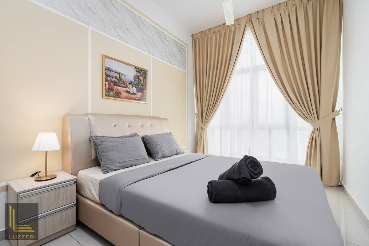 Une chambre d’hôtel avec un lit, une table de chevet, une lampe, un tableau au mur et des rideaux beiges.