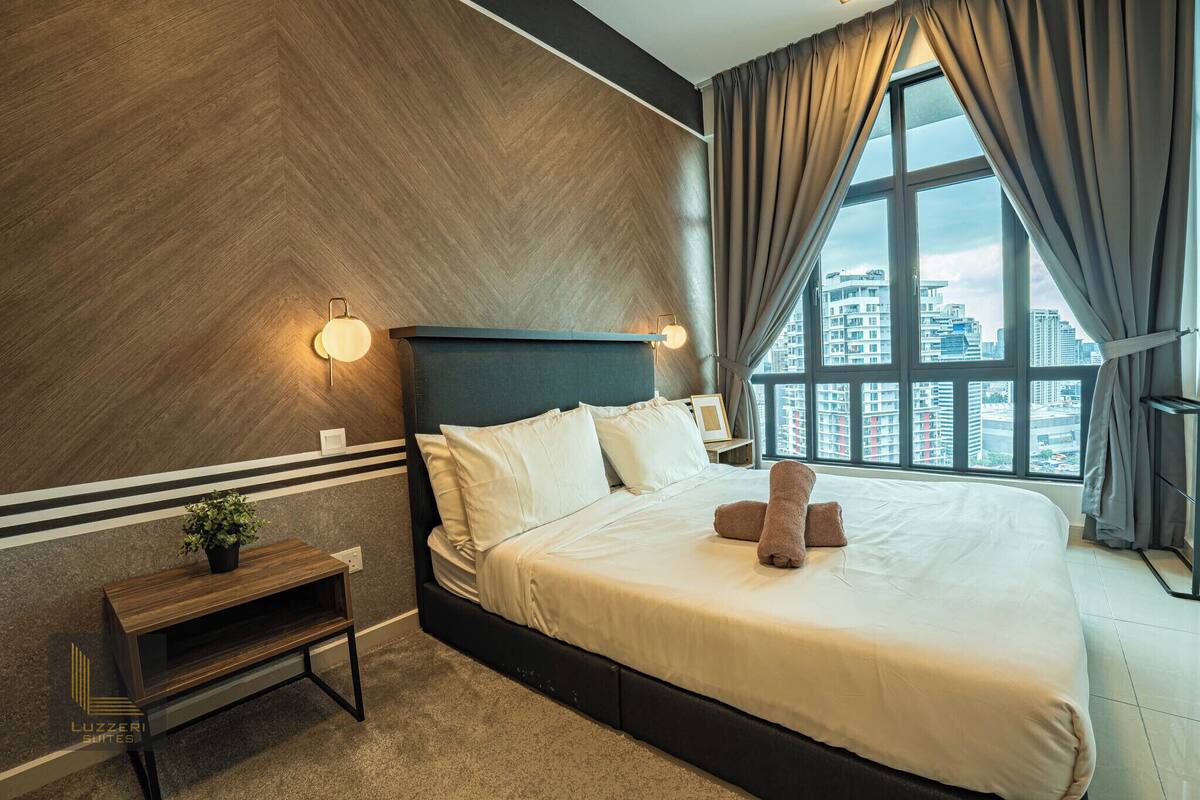 Une chambre d’hôtel moderne avec un grand lit, une table de chevet, une plante en pot et une vue sur la ville par une grande fenêtre.