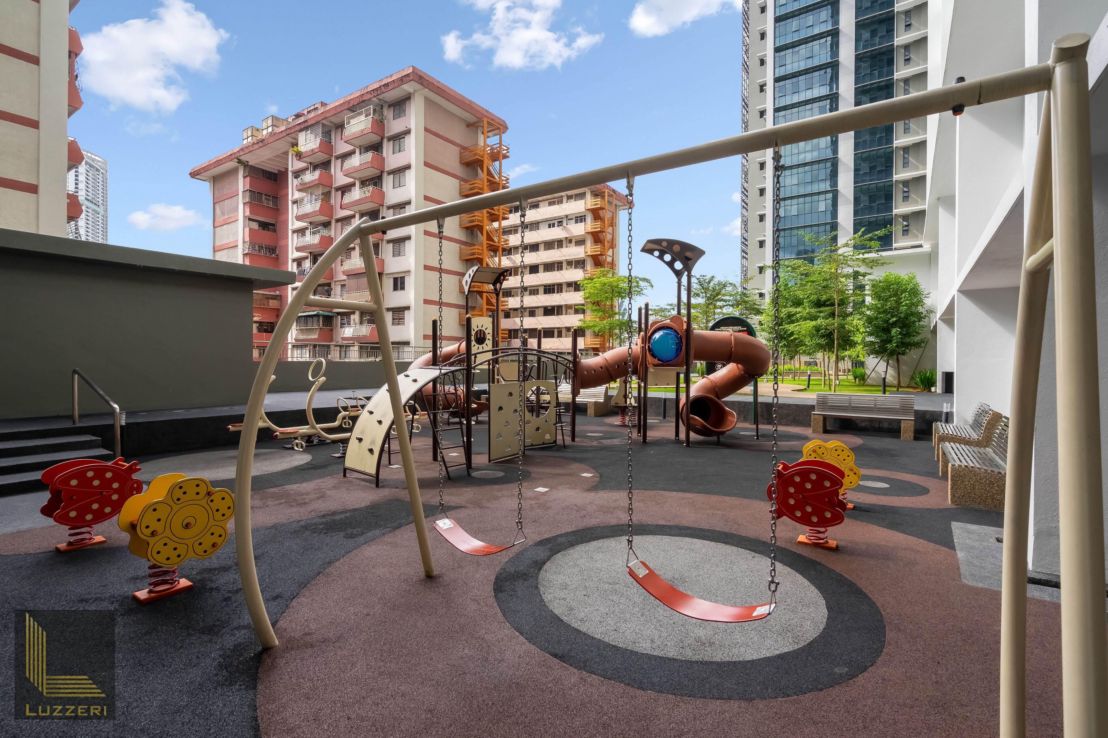 An outdoor playground with swings, slides, and climbing structures, surrounded by a building with balconies.