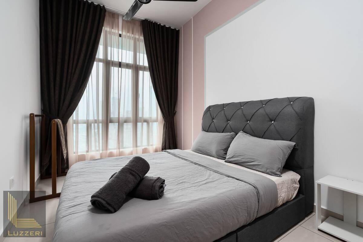 Une chambre à coucher moderne avec une tête de lit capitonnée, une literie grise et une serviette soigneusement pliée posée sur le lit.