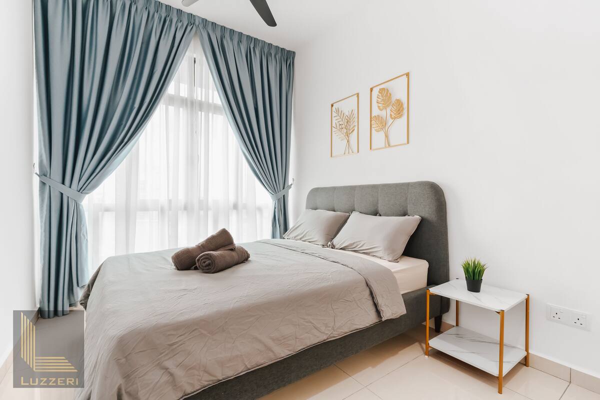 Une chambre à coucher moderne avec un lit, des rideaux, une table de chevet agrémentée d’une plante, et deux œuvres d’art encadrées accrochées au mur.