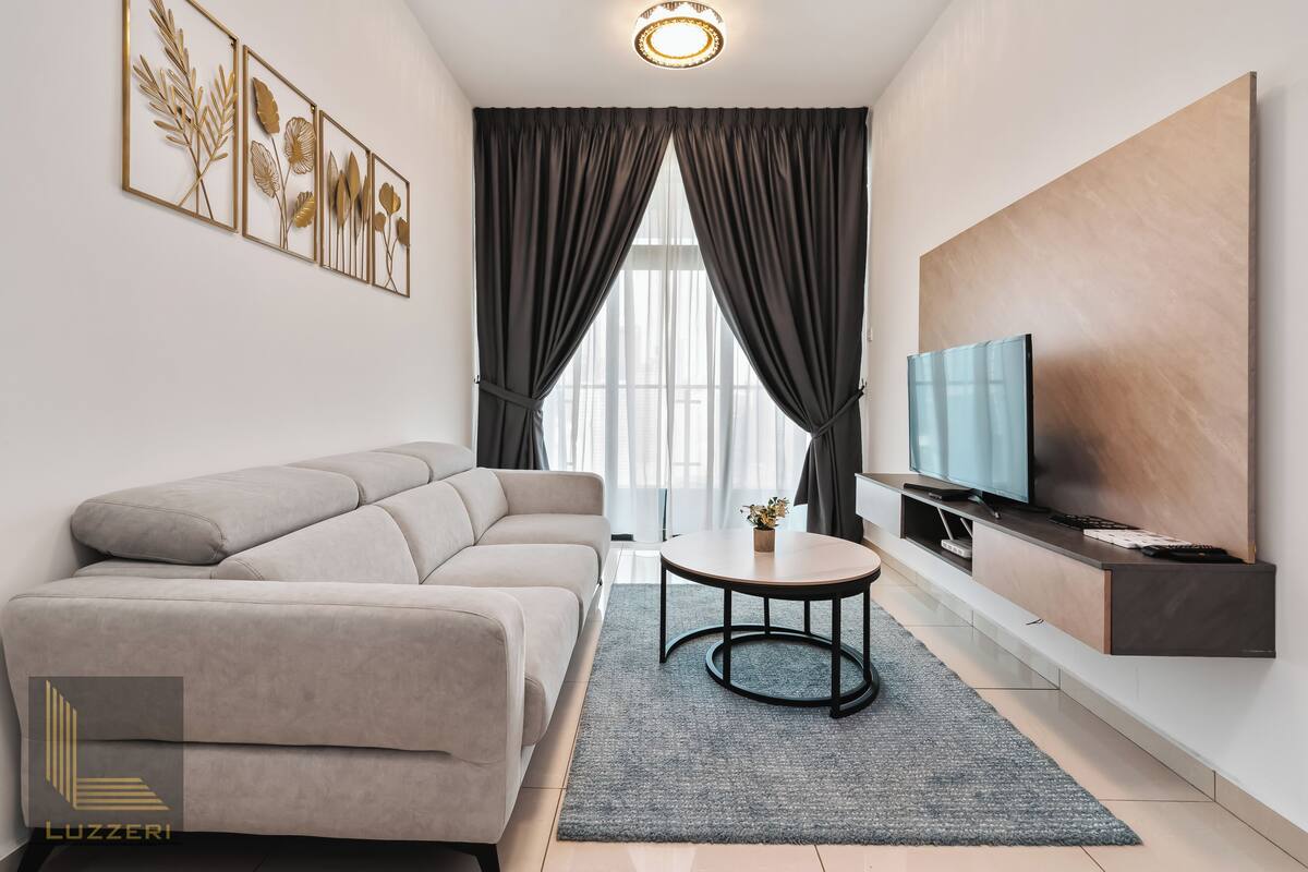 Un salon moderne avec un canapé, une table basse ronde, un téléviseur et une grande fenêtre avec des rideaux.