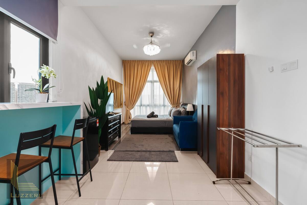 Une chambre moderne et bien éclairée, équipée d’un lit, d’un bureau, de chaises, d’un canapé bleu et d’un étendoir.