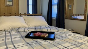 A neatly made bed with a checkered bedspread, a bedside table with a book, and a large mirror on the wall. - Cozy Newmarket Escape! Wine & WiFi! Full Kitchen! (Newmarket)