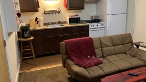 A compact kitchen with a stove, microwave, and sink. A brown couch with a red blanket is in the living area. - Cozy Newmarket Escape! Wine & WiFi! Full Kitchen! (Newmarket)