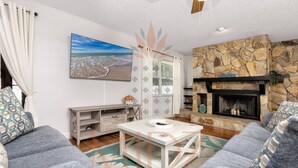 Una sala de estar con sofás grises, una mesa de centro blanca, una chimenea de piedra y un cuadro de una playa.