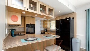 Una cocina moderna con una isla central, dos taburetes de bar, un refrigerador negro y un cubo de basura.