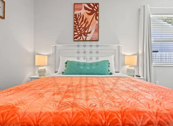 Une chambre d’hôtel avec un grand lit, une tête de lit blanche, deux lampes de chevet, un coussin décoratif vert et une  œuvre d’art accrochée au mur.