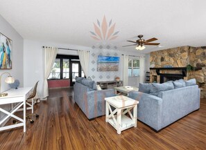 Un salon moderne avec une cheminée en pierre, un ventilateur de plafond et une grande fenêtre avec des rideaux.